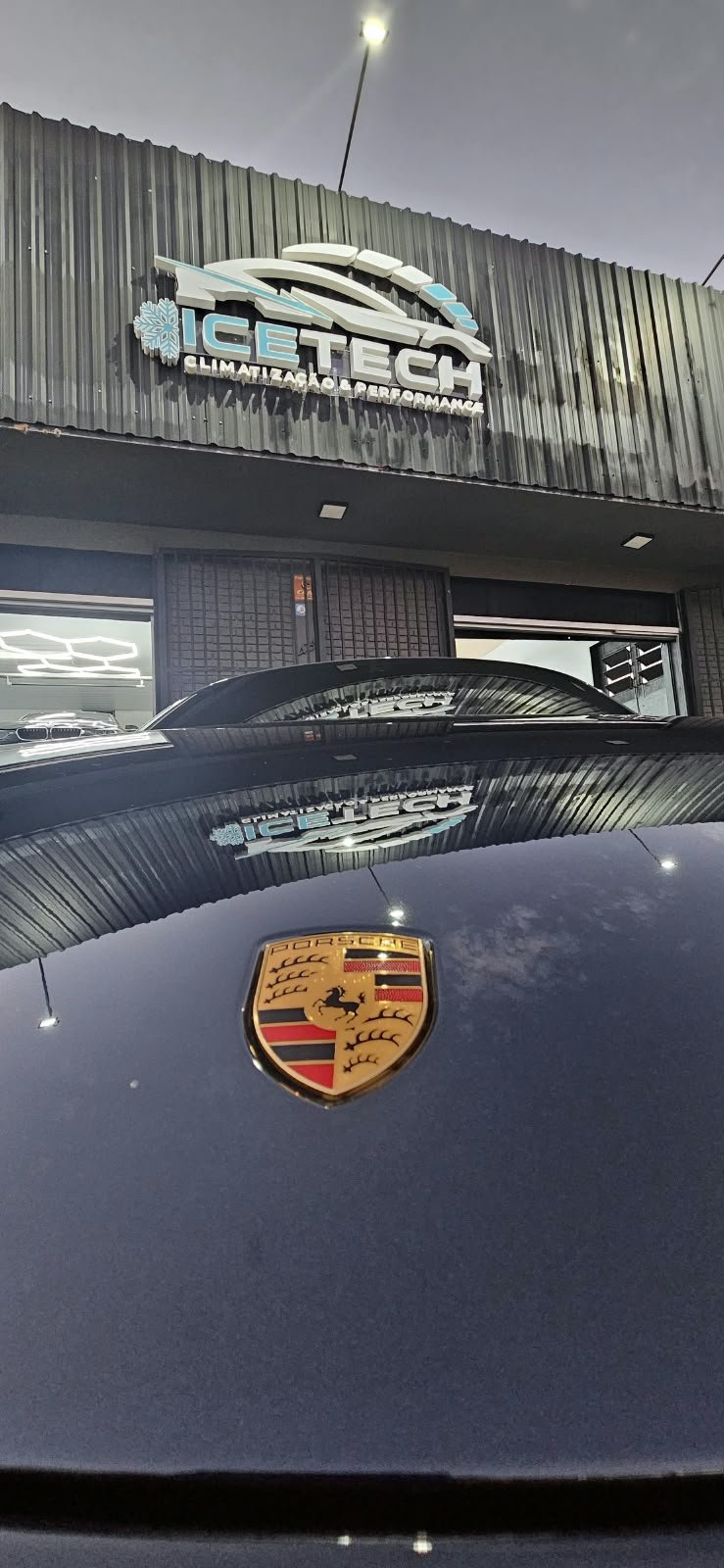 Capô do Porsche com a fachada da ICETECH ao fundo